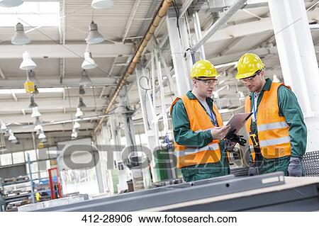 Workers in protective workwear with clipboard in factory View Large Photo Image Stock Photograph - Workers in protective workwear with clipboard in factory. Fotosearch