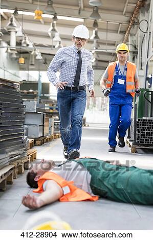 Picture - Workers running toward fallen coworker unconscious on factory floor. Fotosearch