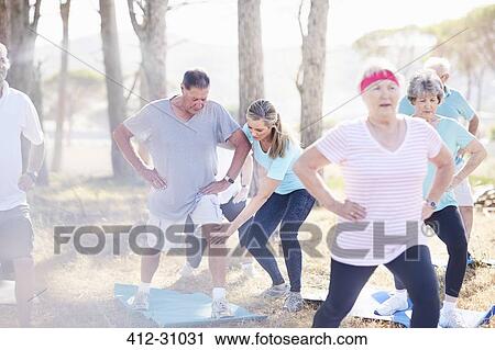 Stock Image - Yoga instructor guiding senior man in sunny park. Fotosearch