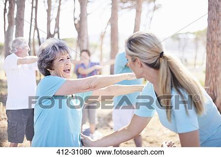 Stock Image - Yoga instructor guiding senior woman in park. Fotosearch