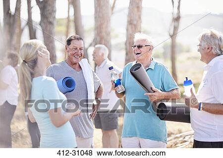 Stock Photo - Yoga instructor talking to senior men after class in park. Fotosearch