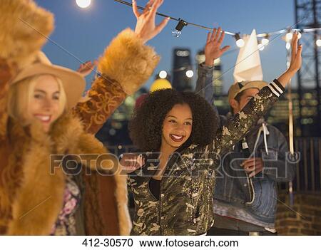 Stock Image - Young adult friends dancing and enjoying rooftop party. Fotosearch