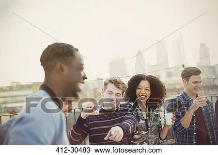 Young adult friends drinking and laughing at rooftop party View Large Photo Image Stock Image - Young adult friends drinking and laughing at rooftop party. Fotosearch