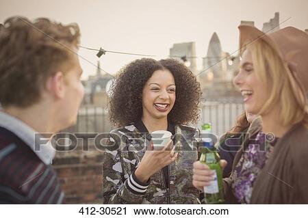 Stock Image - Young adult friends drinking and enjoying rooftop party. Fotosearch