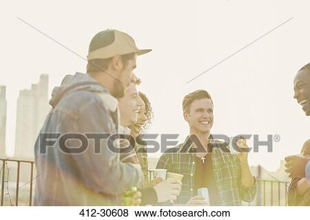 Young adult friends drinking and talking at rooftop party View Large Photo Image Stock Photo - Young adult friends drinking and talking at rooftop party. Fotosearch