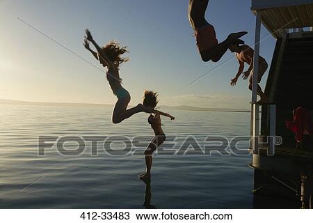 Young adult friends jumping from summer houseboat into sunset ocean View Large Photo Image Stock Image - Young adult friends jumping from summer houseboat into sunset ocean. Fotosearch