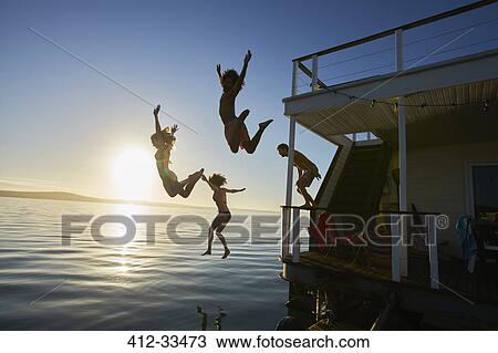 Young adult friends jumping off summer houseboat into sunset ocean View Large Photo Image Stock Image - Young adult friends jumping off summer houseboat into sunset ocean. Fotosearch