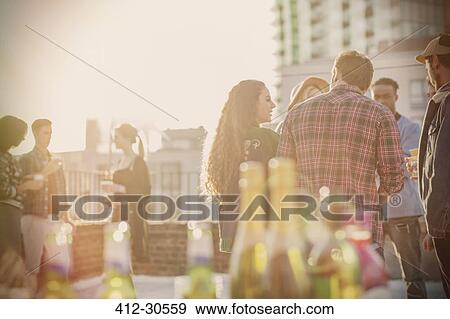 Stock Photo - Young adult friends socializing at sunny rooftop party. Fotosearch