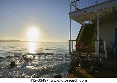 Stock Photo - Young adult friends swimming near summer houseboat on sunset ocean. Fotosearch