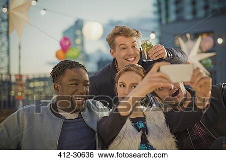 Young adult friends taking selfie at rooftop party View Large Photo Image Stock Photograph - Young adult friends taking selfie at rooftop party. Fotosearch