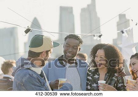 Stock Photo - Young adult friends talking and drinking at rooftop party. Fotosearch