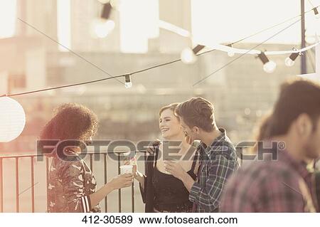Young adult friends talking and drinking at rooftop party View Large Photo Image Stock Photo - Young adult friends talking and drinking at rooftop party. Fotosearch