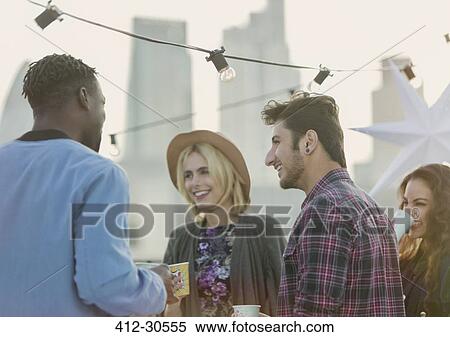 Stock Photography - Young adult friends talking and drinking at rooftop party. Fotosearch