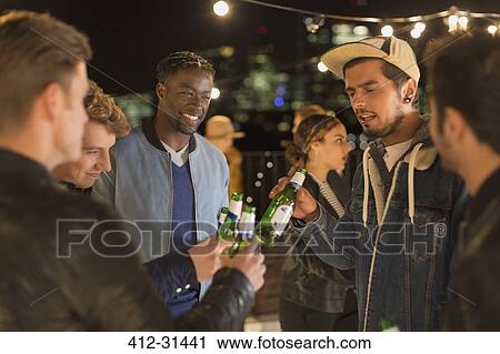 Young adult friends toasting beer bottles at rooftop party View Large Photo Image Stock Image - Young adult friends toasting beer bottles at rooftop party. Fotosearch