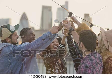 Stock Photo - Young adult friends toasting champagne glasses at rooftop party. Fotosearch