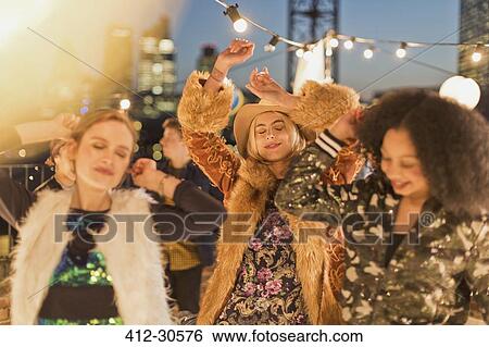 Stock Photograph - Young adult women dancing at nighttime rooftop party. Fotosearch