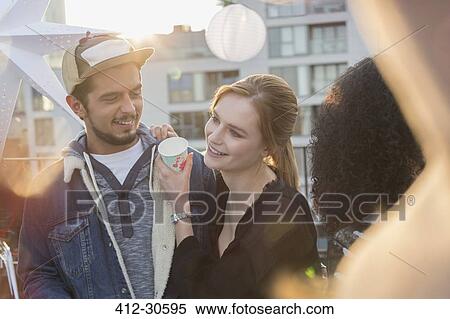 Stock Photography - Young couple drinking and enjoying rooftop party. Fotosearch