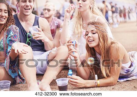 Stock Image - Young friends hanging out blowing bubbles at music festival. Fotosearch
