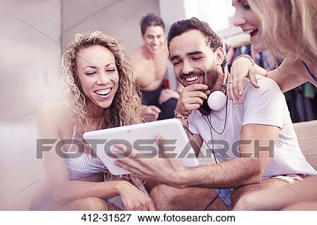 Stock Photo - Young friends laughing using digital tablet. Fotosearch