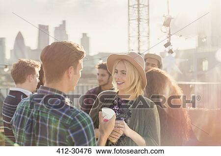 Stock Photograph - Young man and woman drinking and talking at rooftop party. Fotosearch