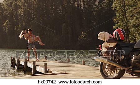Young man carrying young woman on lakeside dock near motorcycle View Large Photo Image Stock Image - Young man carrying young woman on lakeside dock near motorcycle. Fotosearch