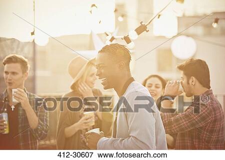 Young man laughing and drinking at rooftop party View Large Photo Image Stock Photo - Young man laughing and drinking at rooftop party. Fotosearch