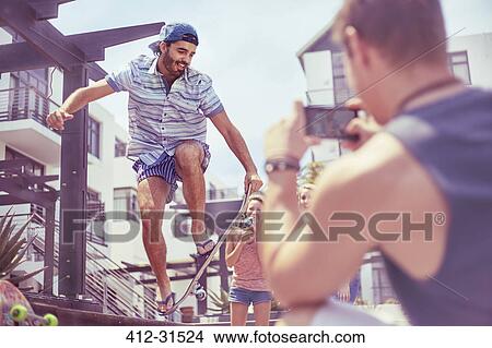 Picture - Young man photographing friend doing skateboard stunt. Fotosearch