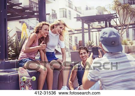 Stock Photograph - Young man photographing friends hanging out. Fotosearch