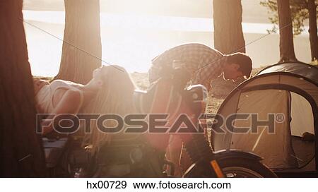 Young man preparing tent at campsite next to woman laying on motorcycle View Large Photo Image Stock Photo - Young man preparing tent at campsite next to woman laying on motorcycle. Fotosearch