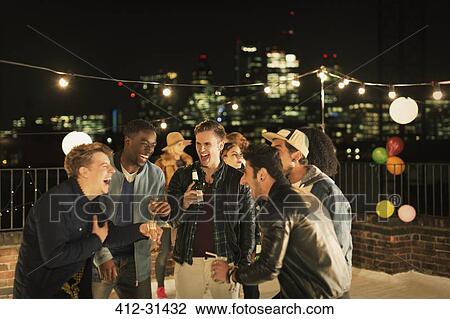 Stock Image - Young men drinking and laughing at rooftop party. Fotosearch