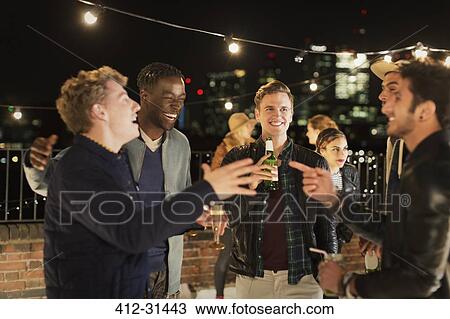 Young men drinking and laughing at rooftop party View Large Photo Image Stock Image - Young men drinking and laughing at rooftop party. Fotosearch