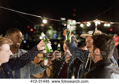 Stock Photography - Young men drinking beer and dancing at rooftop party. Fotosearch