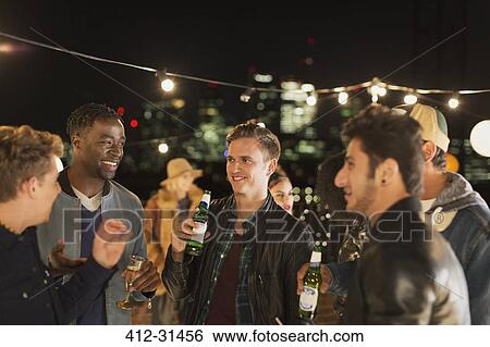 Young men drinking beer and talking at rooftop party View Large Photo Image Stock Photograph - Young men drinking beer and talking at rooftop party. Fotosearch