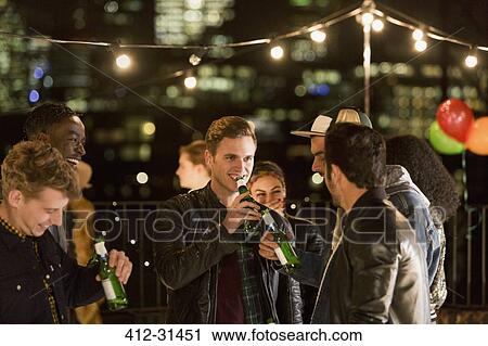 Stock Image - Young men drinking beer at rooftop party. Fotosearch