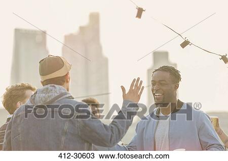 Young men high fiving at rooftop party View Large Photo Image Stock Image - Young men high fiving at rooftop party. Fotosearch