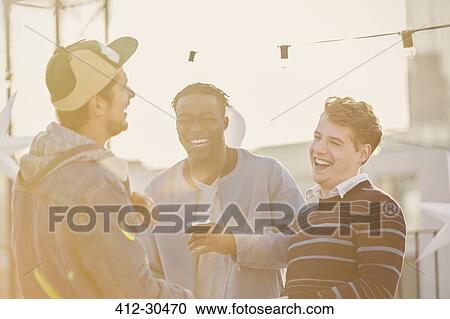 Stock Image - Young men laughing at rooftop party. Fotosearch