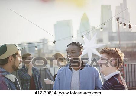 Picture - Young men talking at rooftop party. Fotosearch