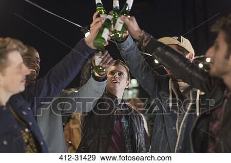 Young men toasting beer bottles at party View Large Photo Image Stock Photo - Young men toasting beer bottles at party. Fotosearch