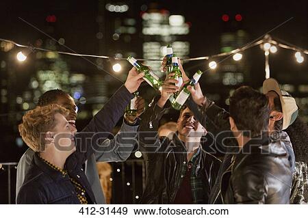 Young men toasting beer bottles at rooftop party View Large Photo Image Stock Photo - Young men toasting beer bottles at rooftop party. Fotosearch