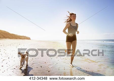 Young woman and dog running on sunny beach View Large Photo Image Stock Photo - Young woman and dog running on sunny beach. Fotosearch