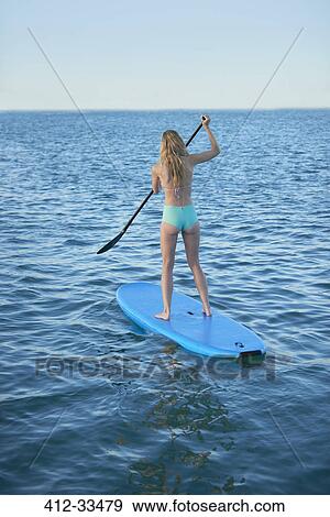 Young woman in bikini paddleboarding in summer ocean View Large Photo Image Stock Photo - Young woman in bikini paddleboarding in summer ocean. Fotosearch