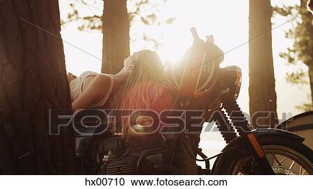 Young woman laying on motorcycle under sunny trees View Large Photo Image Stock Image - Young woman laying on motorcycle under sunny trees. Fotosearch