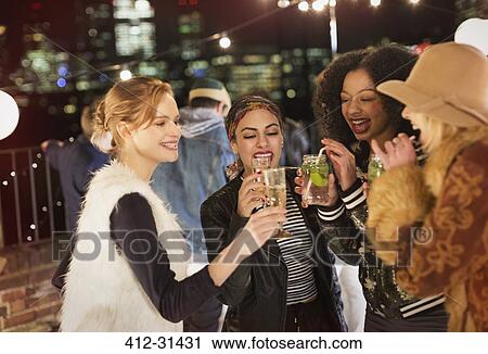 Stock Image - Young women drinking and enjoying rooftop party. Fotosearch