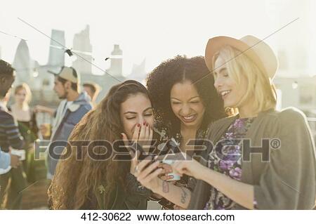 Young women laughing and texting with cell phone at rooftop party View Large Photo Image Stock Image - Young women laughing and texting with cell phone at rooftop party. Fotosearch