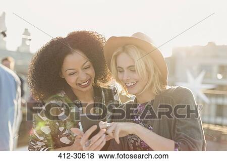 Young women texting with cell phone at rooftop party View Large Photo Image Stock Photo - Young women texting with cell phone at rooftop party. Fotosearch