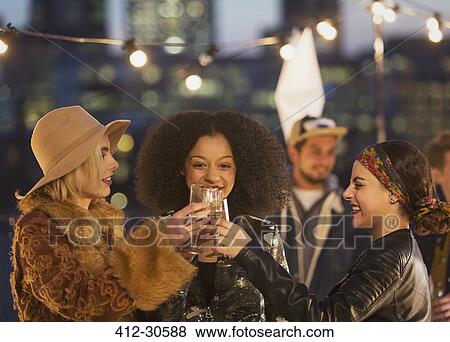Young women toasting champagne glasses at nighttime rooftop party View Large Photo Image Stock Photo - Young women toasting champagne glasses at nighttime rooftop party. Fotosearch