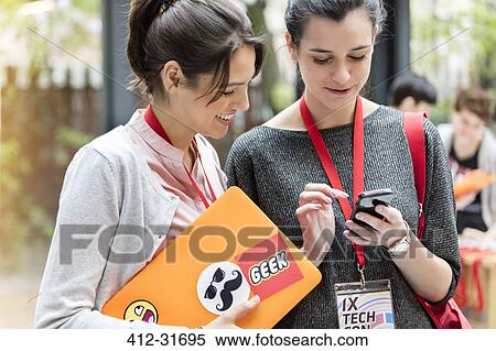 Stock Photography - Young women using smart phone at technology conference. Fotosearch