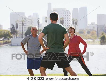 Stock Image - Older couple exercising with trainer in park. Fotosearch