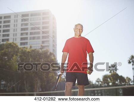 Stock Image - Older man playing tennis on court. Fotosearch