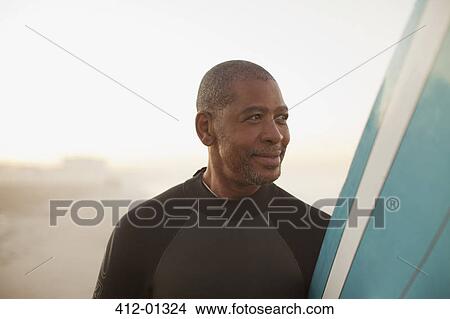 Older surfer carrying board on beach View Large Photo Image Picture - Older surfer carrying board on beach. Fotosearch